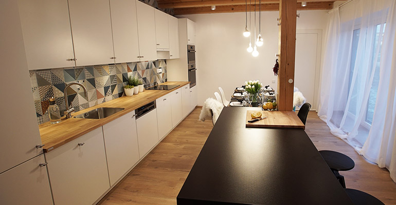 Velká kuchyň, která působí moderním a hřejivým dojmem s dřevěnou pracovní deskou s jídelním koutem
