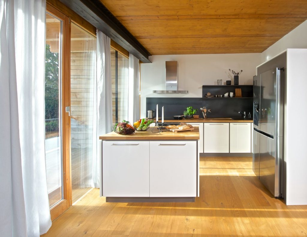 Moderní kuchyňský nábytek v bílé barvě v kombinaci s pracovní deskou, podlahou a stropem v dekoru dřeva