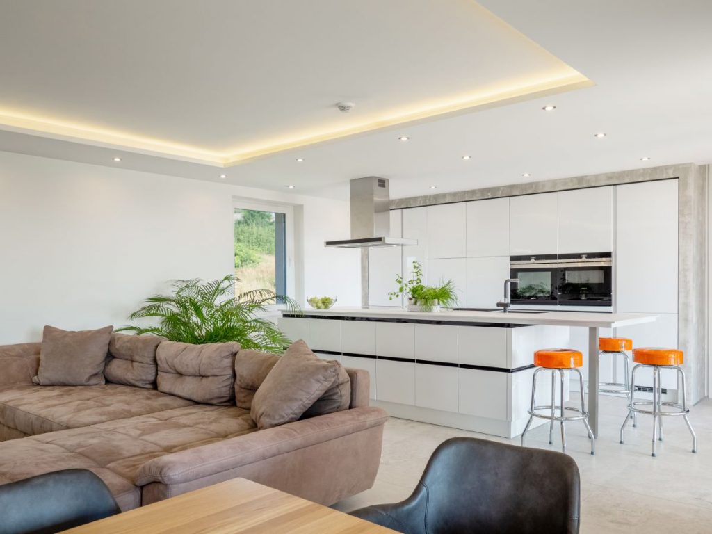 Lesklá kuchyně v moderním stylu s ostrůvek, designovou digestoří a stolem. Kuchyně je propojená s obývákem.