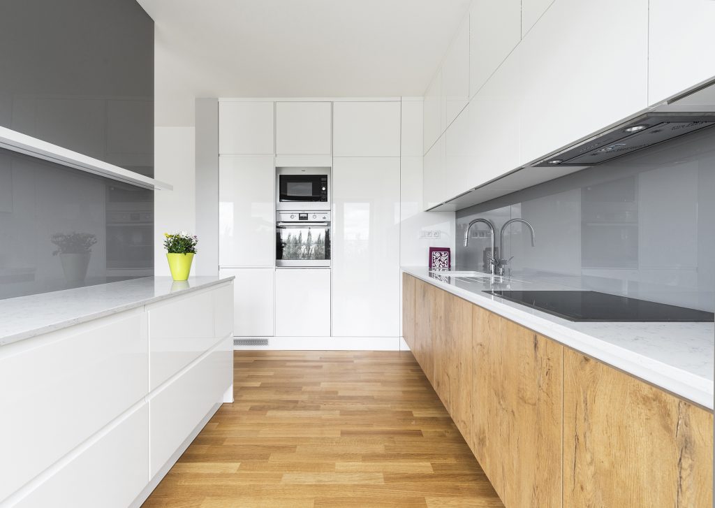 Minimalistická kuchyně v bílé barvě s šedým zádovým panelem a spodními skříňkami v dekoru světlého dřeva.