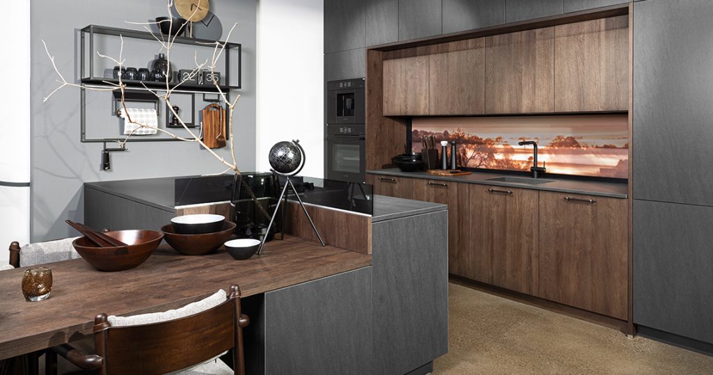 Tmavá kuchyně v moderním stylu s jídelním stolem integrovaným v kuchyňském ostrůvku.