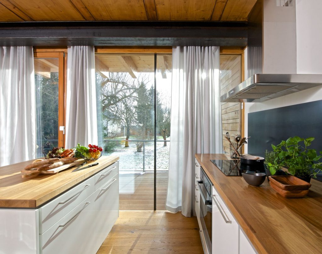 Moderní kuchyně v bílé nadčasové barvě s dřevěnou pracovní deskou s kuchyňským ostrůvkem.