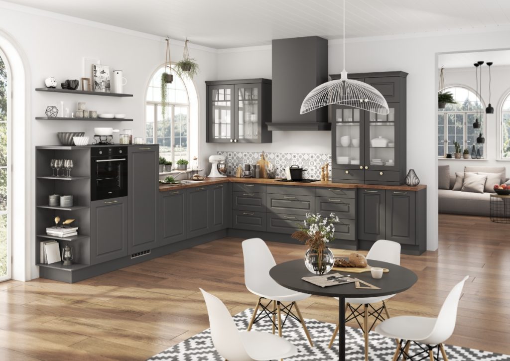 Rohová kuchyně v šedé barvě v provence stylu s dřevěnou pracovní deskou a kulatým jídelním stolem.
